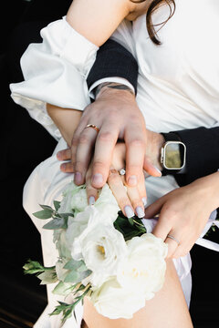 Hand lies on hand, holding wedding bouquet, black background, white dress, bride and groom holding hands. Wedding photography.