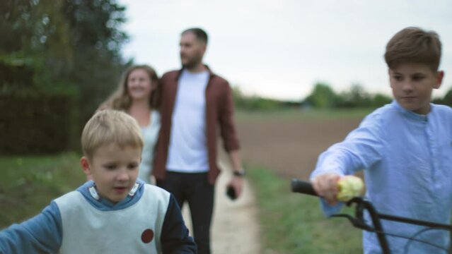 family vacation, active parents with male children having fun while walking on bicycles in countryside on a warm evening