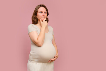 A thoughtful pregnant woman on a pink studio background. Pregnancy in a pensive woman with a belly, copy space