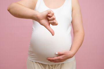 Pregnant woman showing thumbs down gesture, studio pink background