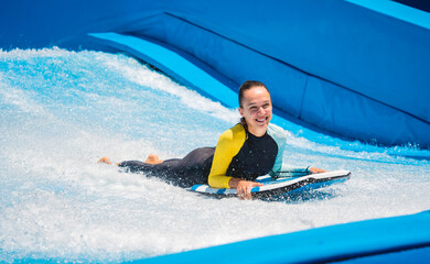 Beautiful young woman surfing on a wave simulator at a water amusement park