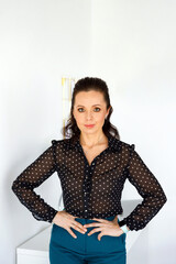 woman in blouse, stands against background of white wall