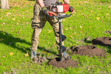 Gardener using tools hand-held soil hole drilling machine or portable manual earth auger.