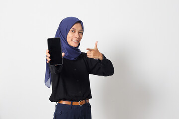 Portrait of excited Asian hijab woman in casual shirt showing blank screen mobile phone mockup while pointing and presenting product. Isolated image on white background