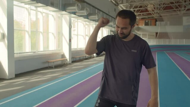 Full length slow motion shot of Caucasian male runner with prosthetic running blade rejoicing after finishing race successfully during training on indoor track