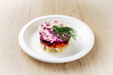 Herring salad under a fur coat on a plate. On a light wooden background.