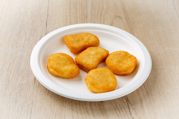 Chicken nuggets on a plate. On a light wooden background.