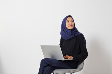 Portrait of excited Asian hijab woman in casual shirt sitting on chair, working on laptop. An employee or student doing her task and job . Businesswoman concept. Isolated image on white background