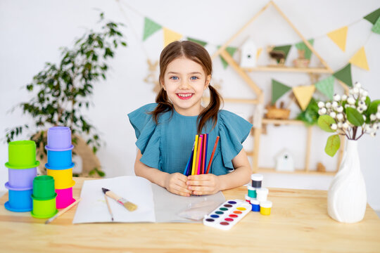 cute little child girl with colorful pencils in her hands in the nursery learning to draw, art lessons with pencils and paints