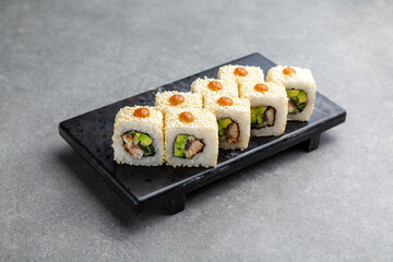 Japanese Sushi roll with eel and avocado on a black stand, gray background