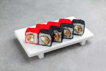 Japanese Sushi roll in black and red caviar on a white stand, gray background