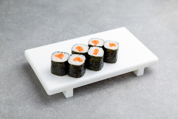 Japanese Sushi roll maki with salmon on a white stand, gray background