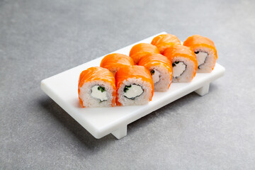 Japanese Sushi roll Philadelphia with green onions on a white stand, gray background