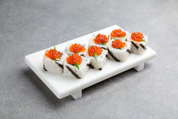 Japanese Sushi roll with red caviar on a white stand, gray background