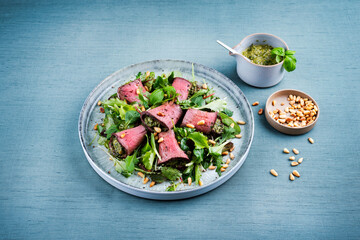 Traditioneller gemischter Salat mit Spinat gefüllten Roastbeef Röllchen und Pinienkerne serviert als Nahaufnahme auf einem Design Teller mit Textfreiraum 