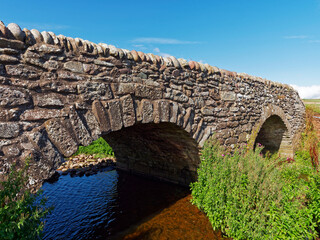 Fototapeta na wymiar An old restored double arched stone footbridge spanning a small burn at the Haughs of Benholm on the Aberdeenshire Coastal Path.