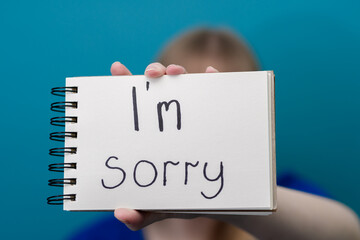 Dziecko trzyma biała kartkę z tekstem, z napisanym odręcznie słowem przepraszam - obrazy, fototapety, plakaty