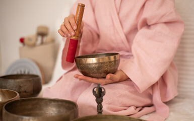 Woman in pink clothes hold metal bells and make music in solon. Indoors. Yoga for health, relaxation and meditation body, practice for forgiveness and spiritual harmony.