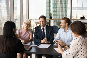 Team of cheerful colleagues having fun on office meeting, laughing, sitting at table in co-working, smiling, laughing, discussing creative ideas, brainstorming, enjoying communication, teamwork