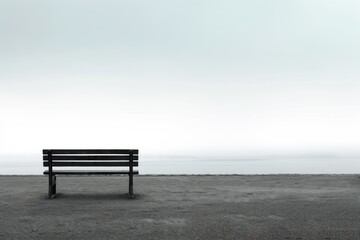 Amidst the misty fog, a wooden bench sits serenely on the beach, a quiet witness to the ever-changing landscape of the sky and sea