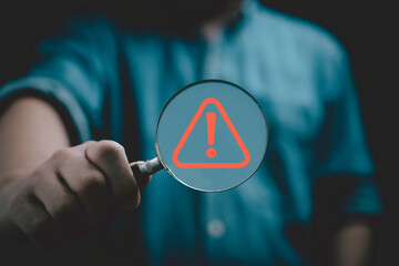 Businessman holding magnifier glass with red triangle caution warning sign for notification error and maintenance concept.