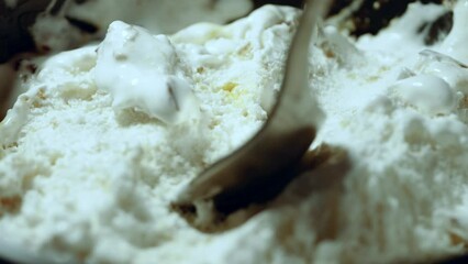 A man scoops up soft creamy ice cream with additives with a spoon. Close-up static shot, with only a plate of dessert in the frame.
