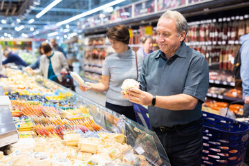 Older man picking out fresh cheese to buy in grocery store