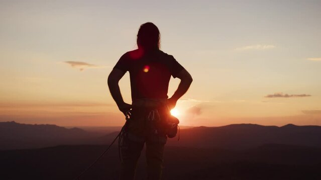 A rock climber finally reaches his destination at the top of the cliff and enjoys sunset