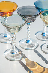 Crystal colorful stemware set with reflection over white background. Colourful elite set of empty alcohol liquor glasses on white, border design. Stemmed glasses, drinkware