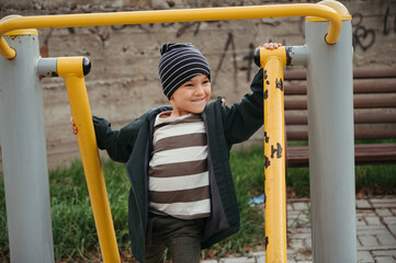 Fototapeta premium Happy child boy playing on horizontal bars on the playground in autumn