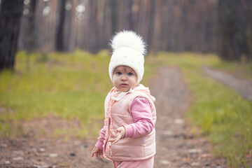 girl baby in a white hat walks in the spring forest