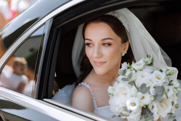 The bride looks out of the car window. Close-up portrait of a pretty shy bride in a car window. Bride smile emotions