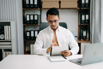 Obraz premium .Young handsome business man working at office with laptop, tablet and taking notes on the paper.