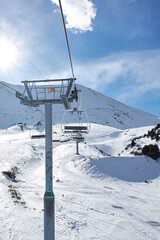 Fototapeta na wymiar Ski lift pole with empty chairs at winter resort. Sunny day, blue sky. Mountain slope. Ropeway construction. Winter vacation activity. Chunkurchak, Bishkek, Kyrgyzstan