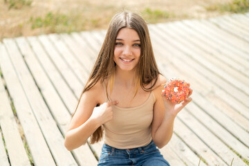 Teenager girl holding a donut at outdoors with surprise facial expression