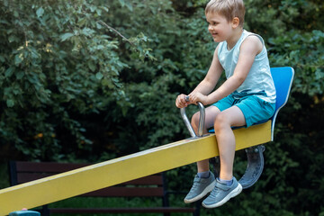 A little boy in blue clothes on a balance swing is very happy because he is up high