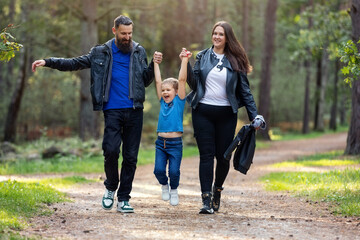 Mother and father lift their son up by the arms during a walk in the forest path. An active child likes such a game, he has fun. Nice day, happy family