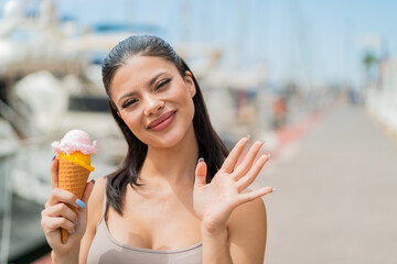 Young pretty woman with a cornet ice cream at outdoors saluting with hand with happy expression