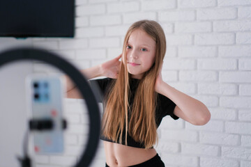 Beautiful teenage girl posing in front of a phone on a tripod. Child blogger shoots video in front...
