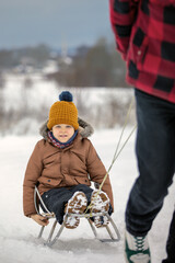 Dad sleds the child in winter. Active walks in winter for children. Father is pulling child on sled. Walking on frosty winter day outdoors