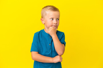 Little Russian boy isolated on yellow background having doubts