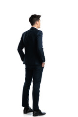 back view of elegant young man holding hands in pockets and standing