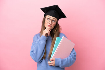 Young student woman wearing a graduate hat isolated on pink background and looking up
