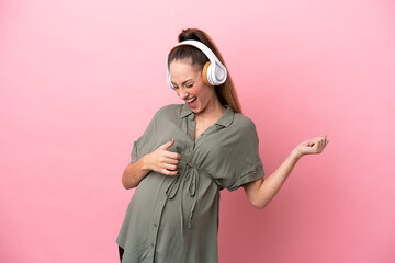 Young woman isolated on pink background pregnant and listening music
