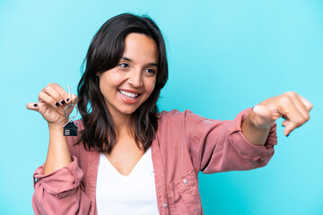 Young hispanic woman holding home keys isolated on blue background giving a thumbs up gesture