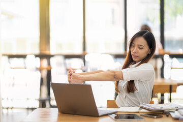 A female employee stretching lazy at the desk to relax while working in the office. Feeling stressed and achy from work.