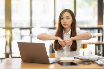 Obraz premium A female employee stretching lazy at the desk to relax while working in the office. Feeling stressed and achy from work.
