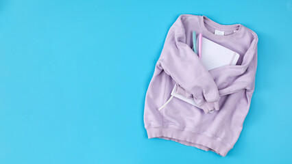 Lilac children's sweatshirt with a notebook on a blue. Copy space