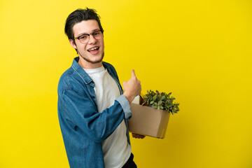 Russian Man making a move while picking up a box full of things isolated on yellow background...