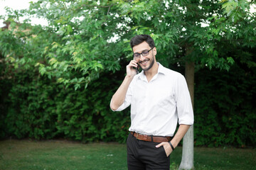 Close up portrait of handsome bearded businessman in official wear talking on mobile phone outdoors	